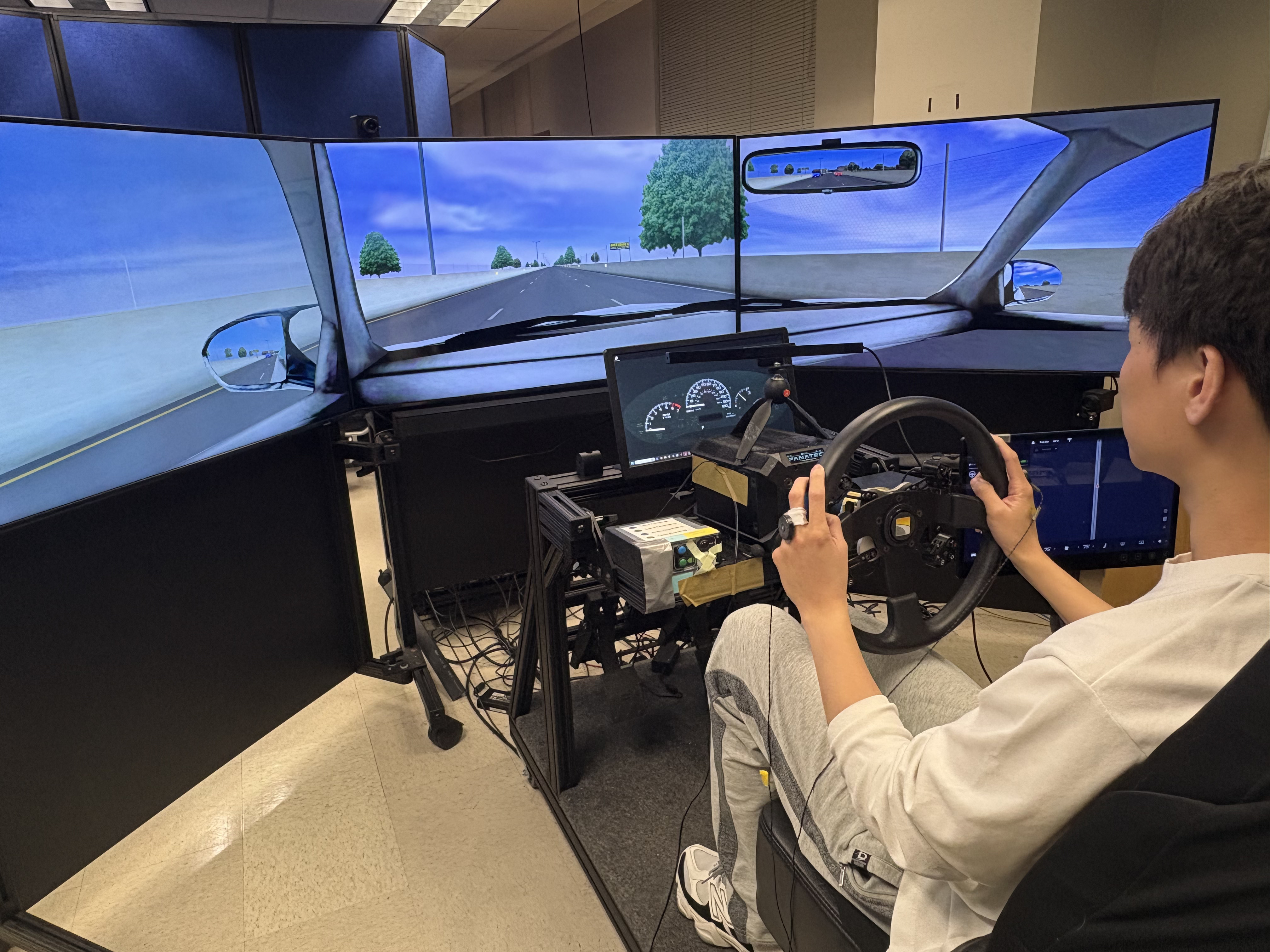 Driving simulator setup with three-screen highway scene and steering wheel